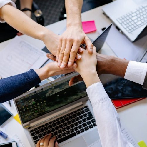 A diverse group of professionals stacking hands over a table symbolizing teamwork and collaboration.
